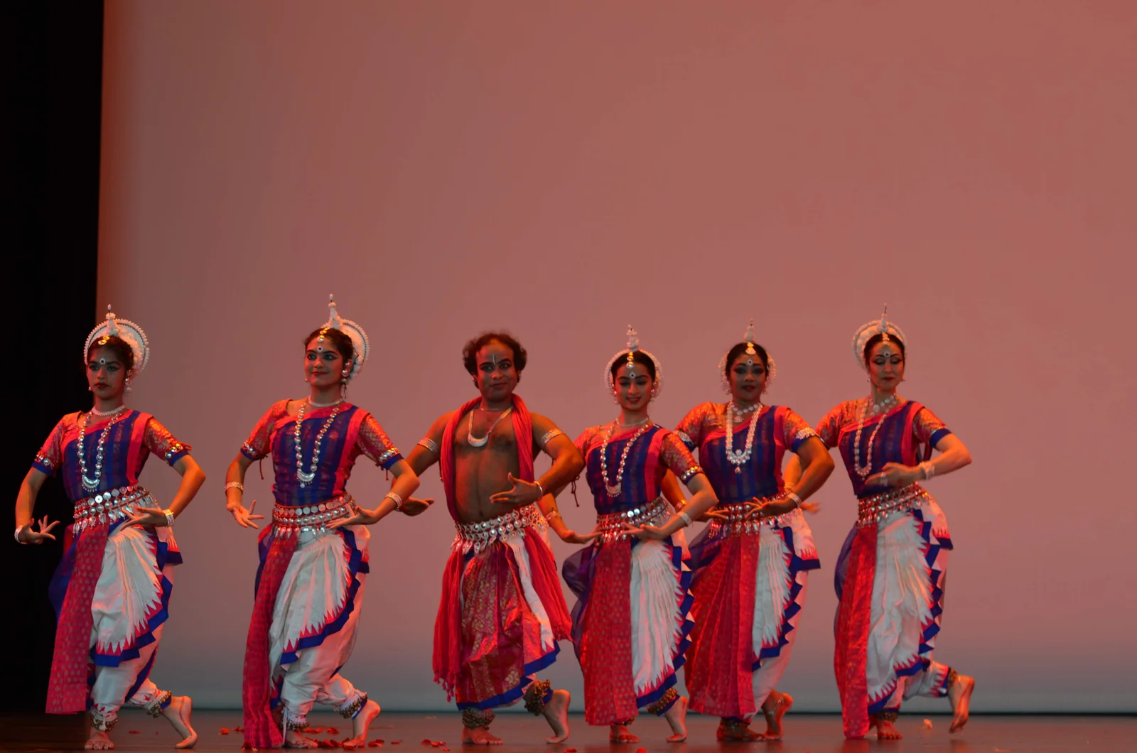 Odissi dancers in traditional attire with intricate jewelry, captured mid-performance on a decorated stage