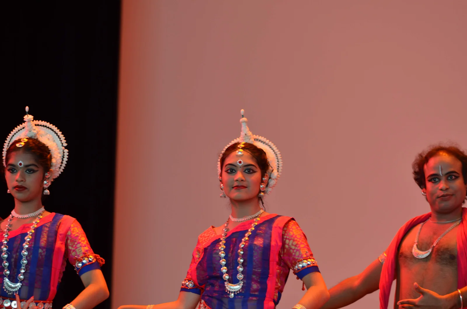 Group of Odissi dancers in traditional attire performing a synchronized dance on a decorated stage.
