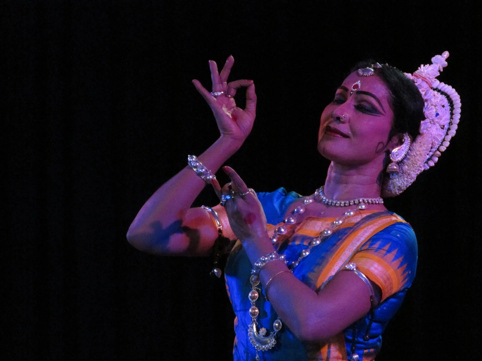 Odissi dancers in traditional attire performing with expressive hand gestures on a decorated stage.