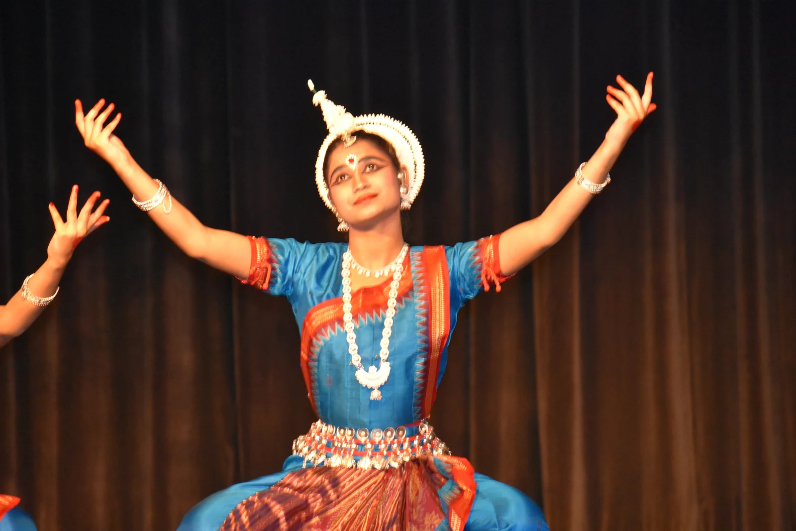 Odissi dancer in traditional attire and intricate jewelry performing a graceful movement on a decorated stage