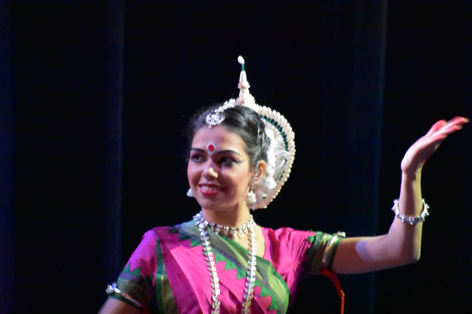 Odissi dancer in vibrant traditional attire and intricate jewelry, striking a graceful pose on a decorated stage