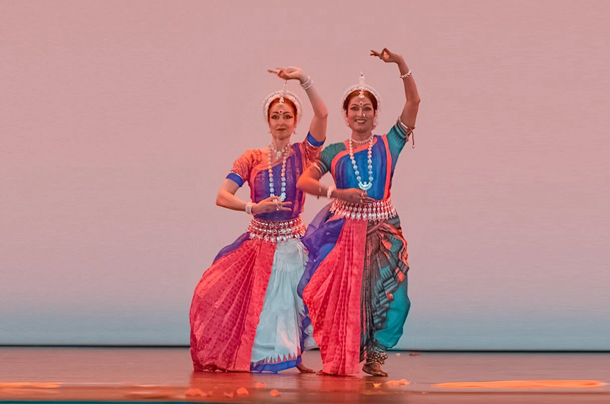 Two Odissi dancers in vibrant traditional attire gracefully performing synchronized poses on stage